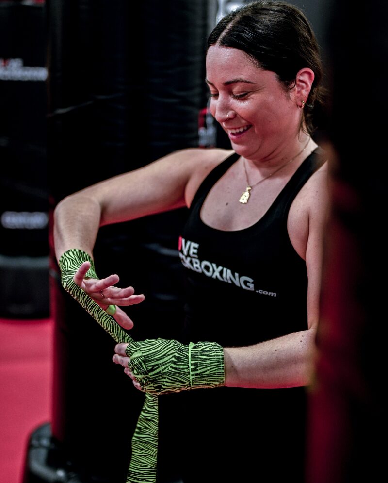 A person preparing for an I Love Kickboxing workout by wrapping their hands with a green tiger stripe wrap.